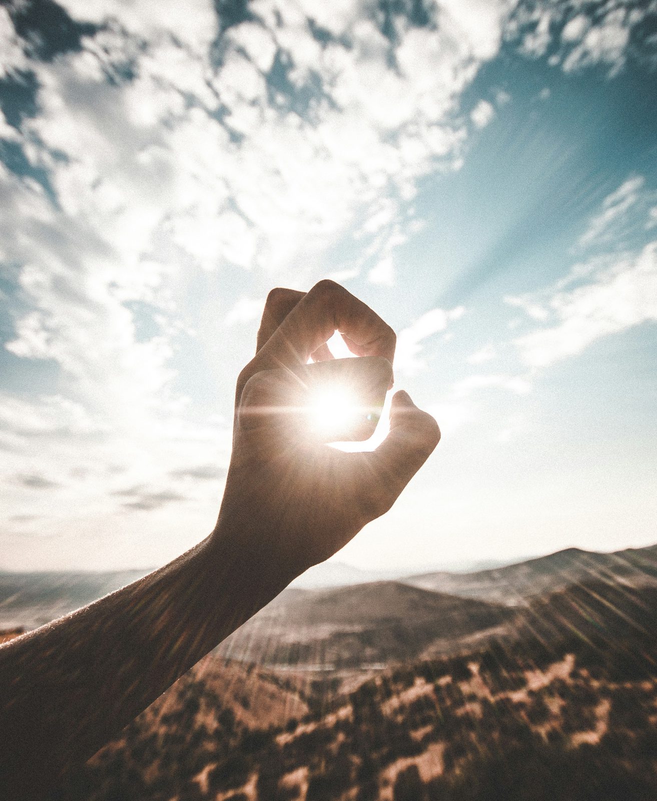 A hand reaching toward warm sunlight at golden hour